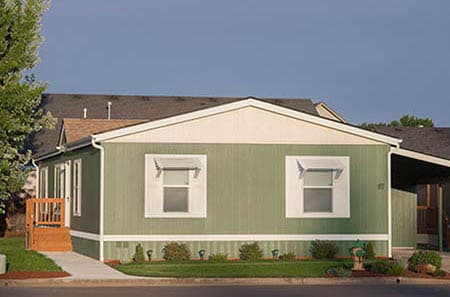 Double-Wide green manufactured home with carport and staircase.